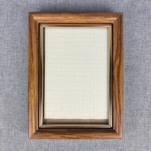 May include: A rectangular wooden picture frame with a light brown finish and a gold-colored inner border. The frame holds a cream-colored paper with a textured surface. The frame is empty, ready for a photo or artwork.
