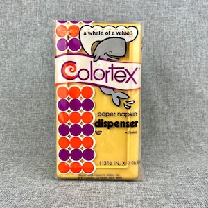 May include: A yellow Colortex paper napkin dispenser in a clear plastic wrapper. The dispenser has a whale graphic and the text "a whale of a value!". The dimensions are 13 1/2 inches by 7 7/8 inches.