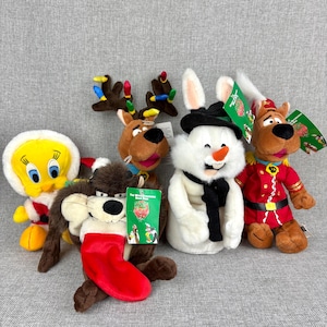 May include: A collection of plush toys featuring cartoon characters. Includes a yellow Tweety Bird, a brown Taz with a red stocking, a brown reindeer, a white snowman, and a brown Scooby-Doo in a red uniform. Each toy has a tag.