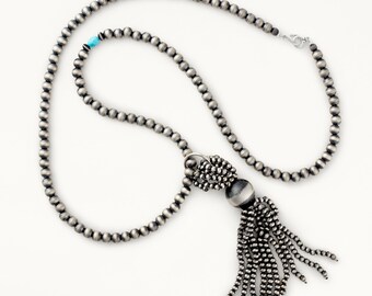May include: A silver necklace with a tassel pendant. The necklace is made of small, round beads and the tassel is made of many strands of beads.