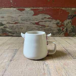 May include: White ceramic mug with red and blue accents on the handles and side. The mug has a rounded shape and a handle on the right side.