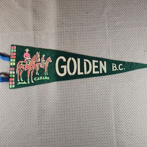 Könnte beinhalten: Ein grünes Filzbanner mit dem Wort "GOLDEN B.C." in weißen Buchstaben. Das Banner zeigt eine Illustration von Reitern auf Pferden und das Wort "CASAIA" in Weiß. Blaues Band ist befestigt.