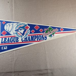 May include: A triangular pennant with the Toronto Blue Jays logo and the text "American League Champions" and "1991 World Series." The pennant is blue, white, and red, with maple leaf designs. Made in the USA.