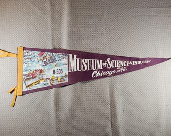 May include: A vintage purple pennant with the text "MUSEUM of SCIENCE & INDUSTRY Chicago, Ill." and an illustration of boats on water. The pennant is mounted on a wooden frame with yellow accents. The pennant also has the text "U-505".