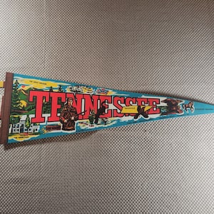 Op de afbeelding: Een vintage wimpel met het woord "Tennessee" in grote rode letters. De vlag toont illustraties van een soldaat, een beer en andere bezienswaardigheden van Tennessee. Het woord "Pennant" staat aan de linkerkant.