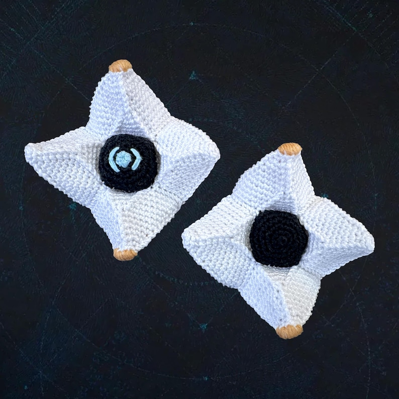 Pode incluir: Duas figuras de fantasmas de croch&ecirc; branco com olhos pretos e azuis. As figuras est&atilde;o sobre um fundo azul escuro.