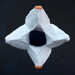 Pode incluir: Um objeto em forma de estrela crochetado em branco com um centro preto. A estrela tem seis pontas e &eacute; crochetada com fio branco. O centro &eacute; um c&iacute;rculo preto.