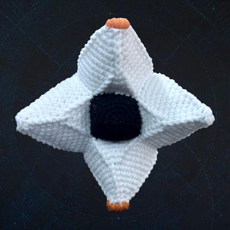 Pode incluir: Um objeto em forma de estrela crochetado em branco com um centro preto. A estrela tem seis pontas e &eacute; crochetada com fio branco. O centro &eacute; um c&iacute;rculo preto.