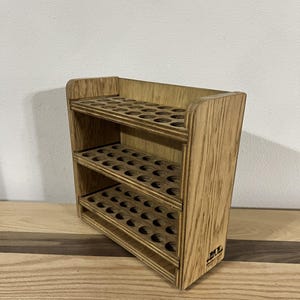 May include: A wooden paint rack with three shelves, each with 12 circular holes for holding paint bottles. The rack is made of light brown wood and has a natural finish. The rack is labeled "DIY" on the bottom.