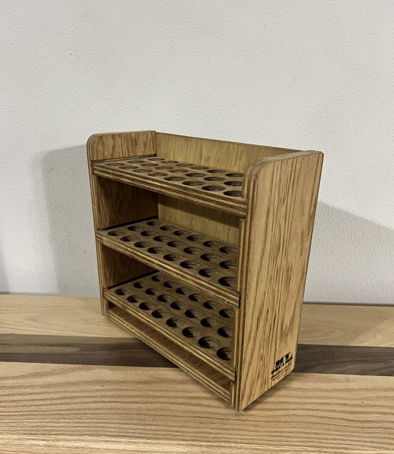 May include: A wooden paint rack with three shelves, each with 12 circular holes for holding paint bottles. The rack is made of light brown wood and has a natural finish. The rack is labeled "DIY" on the bottom.