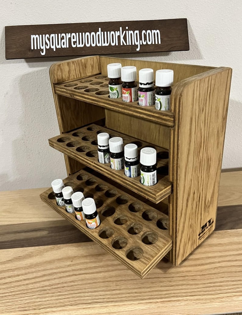 May include: Wooden essential oil rack with three shelves and a pull-out drawer. The rack is made of light brown wood and has a natural wood finish. The rack is filled with small glass bottles of essential oils.