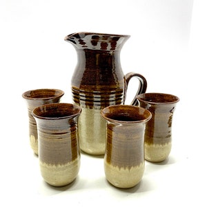 Può includere: Set di cinque pezzi in ceramica marrone e beige, tra cui una brocca e quattro tazze.