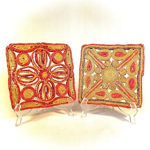 Puede incluir: Dos posavasos cuadrados tejidos con un diseño geométrico rojo y amarillo. Los posavasos se muestran en soportes de acrílico transparente.