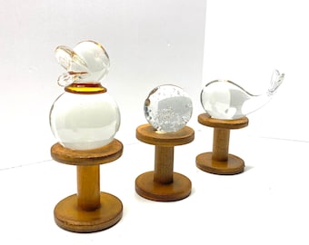 May include: Three glass figurines on wooden stands. The figurines are a duck, a whale, and a sphere. The duck and whale are clear glass, while the sphere has a cloudy appearance.