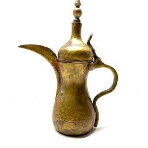 May include: A brass Arabic coffee pot with a decorative handle and a spout. The pot has a round body with intricate engravings and a small knob on the lid.