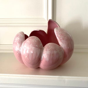 May include: A pink ceramic flower pot with a unique, organic shape. The pot has a glossy finish and white speckles throughout.