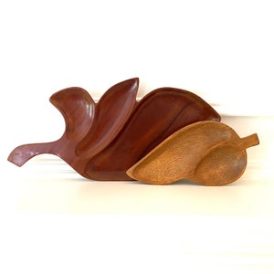 Pode incluir: Um conjunto de três pratos de servir de madeira em forma de folhas. Os pratos são feitos de madeira marrom escura e estão empilhados um em cima do outro.