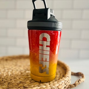 May include: A red and yellow ombre shaker bottle with a black lid and a silver inscription that reads "CHEERS".