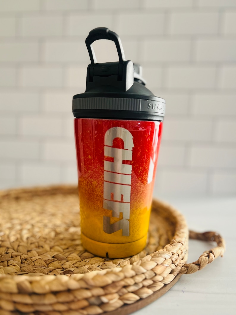May include: A red and yellow ombre shaker bottle with a black lid and a silver inscription that reads "CHEERS".