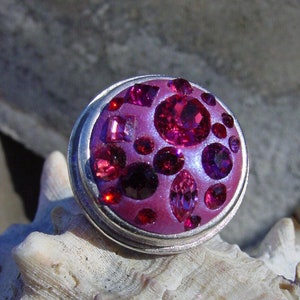 May include: A silver ring with a pink base and a cluster of purple and pink rhinestones.
