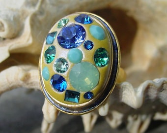May include: A gold ring with a yellow base and a variety of blue, green, and turquoise gemstones.