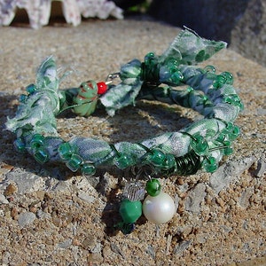 May include: A green and white fabric bracelet with green glass beads and a white pearl charm.