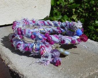Pulsera de alambre con memoria recubierto de tela de color violeta reciclado con cuentas de semillas de frambuesa mate y dijes en los extremos, pulsera de tela
