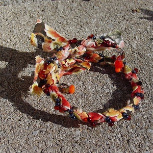 Può includere: Un braccialetto fatto a mano con un design a forma di fiocco. Il braccialetto è realizzato in tessuto colorato nelle tonalità del rosso, arancione, giallo e marrone, ed è adornato con piccole perline rosse e blu scuro. Il braccialetto ha una circonferenza di circa 18 cm.