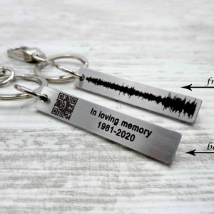 Könnte beinhalten: Silberner Schlüsselanhänger mit einem rechteckigen Anhänger, der auf der Rückseite mit "In loving memory 1981-2020" graviert ist und auf der Vorderseite eine Schallwelle und einen QR-Code.
