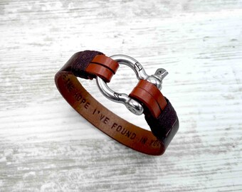 May include: A brown leather bracelet with a silver clasp. The bracelet has the words "The hope I've found in you" engraved on it.