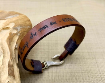 May include: Brown leather bracelet with a silver hook clasp. The bracelet is engraved with the text "Keep the music alive - Keith"