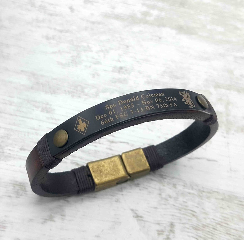 Puede incluir: Un brazalete de cuero negro con cierre dorado y texto grabado: "Spc Donald Coleman Dec 01. 1985 - Nov 06, 2014 66th FSC 3-13 BN 75th FA".