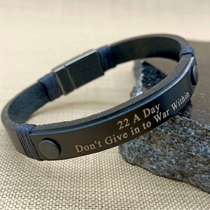Puede incluir: Pulsera de cuero negro con cierre plateado y texto grabado: "22 A Day Don't Give in to War Within"