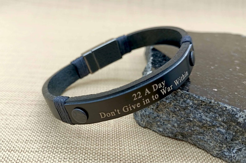 Puede incluir: Pulsera de cuero negro con cierre plateado y texto grabado: "22 A Day Don't Give in to War Within"