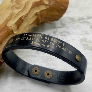 May include: Black leather bracelet with gold-tone accents and engraved coordinates and the text "Semper Fi".