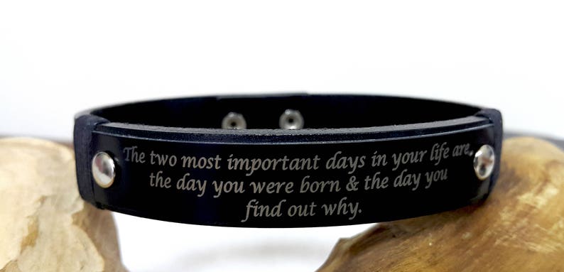 May include: Black leather bracelet with silver studs and an engraved message: "The two most important days in your life are. the day you were born & the day you find out why."
