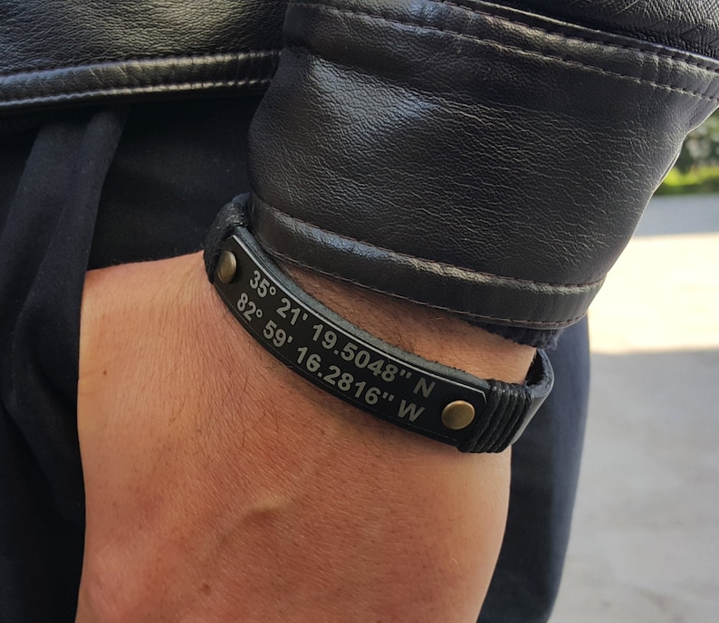 May include: Black leather bracelet with a gold buckle and engraved coordinates: 35&deg; 21' 19.5048" N 82&deg; 59' 16.2816" W