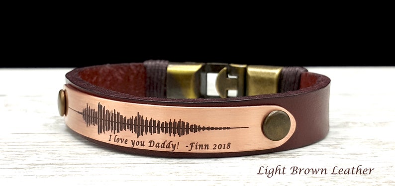 May include: A brown leather bracelet with a copper plate engraved with a sound wave and the text "I love you Daddy! - Finn 2018". Light Brown Leather.