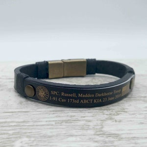 Puede incluir: Pulsera de cuero negro con cierre dorado y texto grabado: "SPC. Russell, Madden Darkhorse Troop 1-91 Cav 173rd ABCT KIA 23 June 2010".