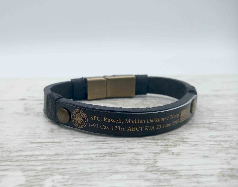 Puede incluir: Pulsera de cuero negro con cierre dorado y texto grabado: "SPC. Russell, Madden Darkhorse Troop 1-91 Cav 173rd ABCT KIA 23 June 2010".