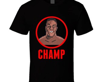 Op de afbeelding: Zwart T-shirt met een rode cirkel met een gepixelde afbeelding van een bokser. De tekst "CHAMP" is in rood onder de cirkel gedrukt.