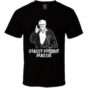 May include: Black t-shirt with a white image of a man with a finger raised and the text "Classy Freddie Blassie".