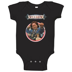 May include: Black baby onesie with a red, white, and blue graphic of the main character from the movie Willow, holding a magic staff. The graphic also includes other characters from the movie. The text "WILLOW" is above the graphic.