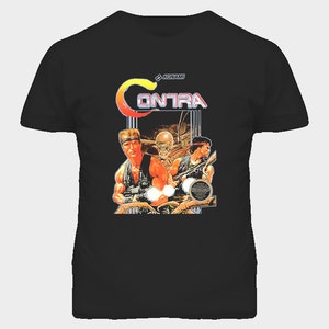 May include: Black t-shirt featuring the Konami Contra video game logo and artwork. The design includes the word "Contra" in a stylized font, along with images of two soldiers and a creature. The Nintendo seal is also visible.