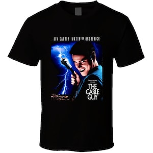 May include: Black t-shirt featuring a movie poster for "The Cable Guy" starring Jim Carrey and Matthew Broderick. The poster shows Jim Carrey holding a cable wire with a lightning bolt behind him.