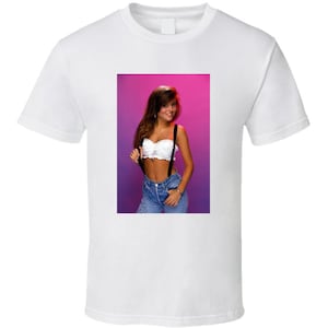 May include: A white t-shirt with a printed image of a woman wearing a white crop top with black suspenders and blue jeans. The woman is standing in front of a pink and purple background.