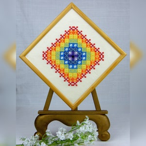 Peut inclure: Un motif de point de croix coloré avec un schéma de couleurs arc-en-ciel, encadré dans un cadre en bois naturel et présenté sur un chevalet en bois.