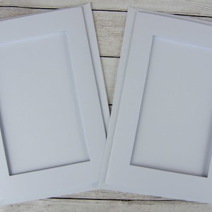 Lot de 2 cartes blanches au point de croix. Cartes à ouverture double avec ouvertures ovales, rectangulaires, carrées ou rondes et enveloppes blanches.