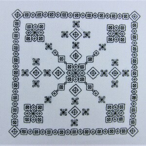 Op de afbeelding: Zwart-wit geometrisch patroon op een witte stoffen achtergrond. Het patroon is symmetrisch en bevat een verscheidenheid aan vormen, waaronder vierkanten, ruiten en sterren.
