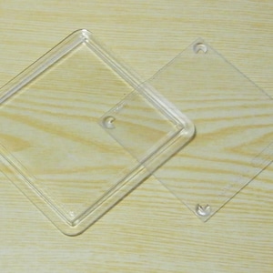May include: Two clear plastic square frames with rounded corners. The larger frame is slightly larger than the smaller frame and has four small holes in the corners. The smaller frame is inside the larger frame.